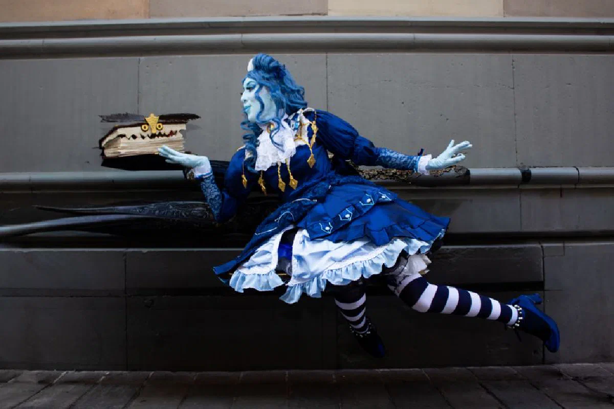 A vibrant blue-themed fantasy cosplay scene featuring a whimsical character with a floating magical book.