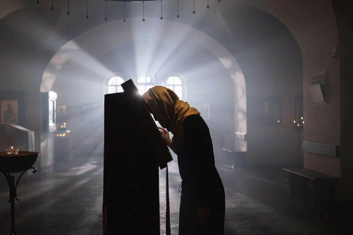 A woman in a shawl prays in a sunlit church, evoking peace and spirituality.