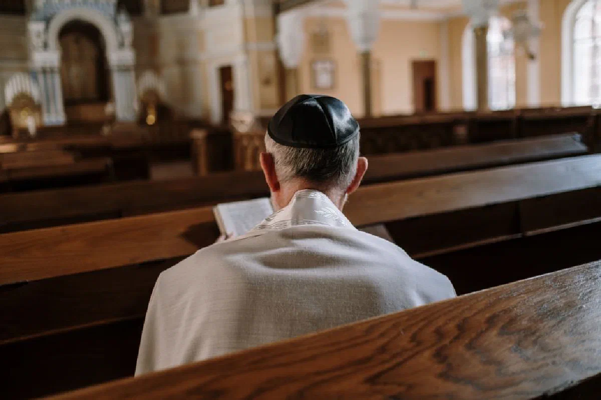 Rear view of a man wearing a tallit and kippah while praying in a synagogue.