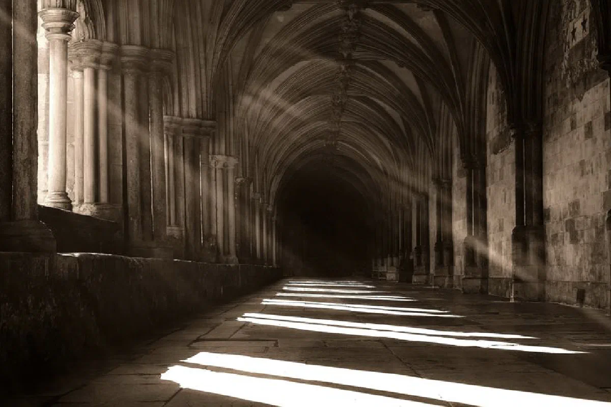 Sunbeams create intriguing shadows in a historical stone hallway, captured in black and white.