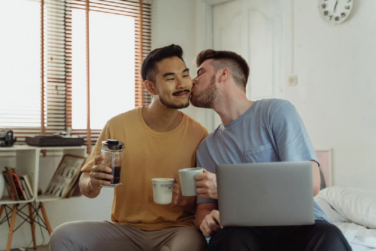 Happy interracial gay couple enjoying morning coffee at home, showing affection and togetherness.