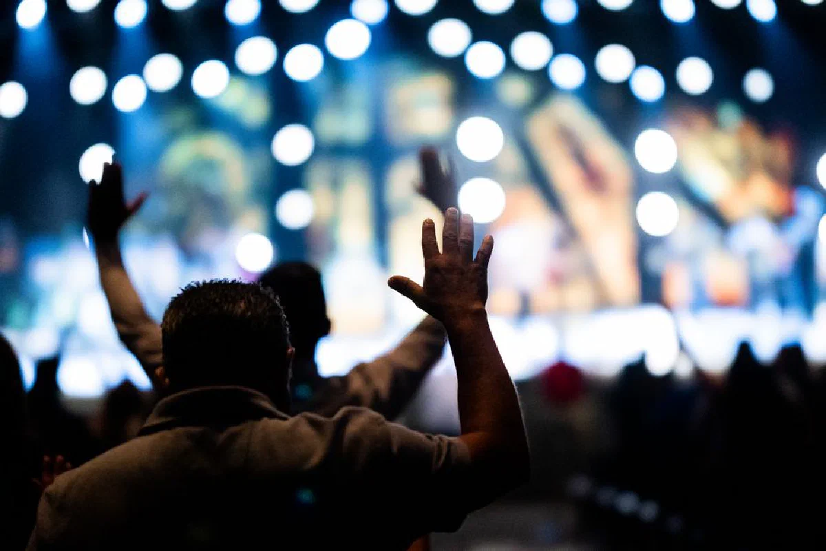 Silhouette of a man raising hands in worship amidst bokeh lights, evoking a sense of spiritual connection.