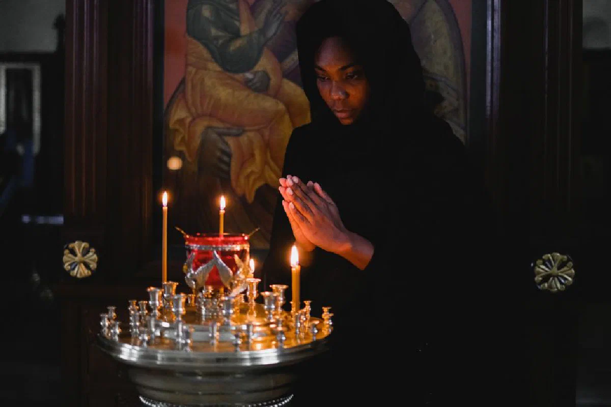 Woman praying with clasped hands in a church, lit by candlelight, evoking spirituality and serenity.