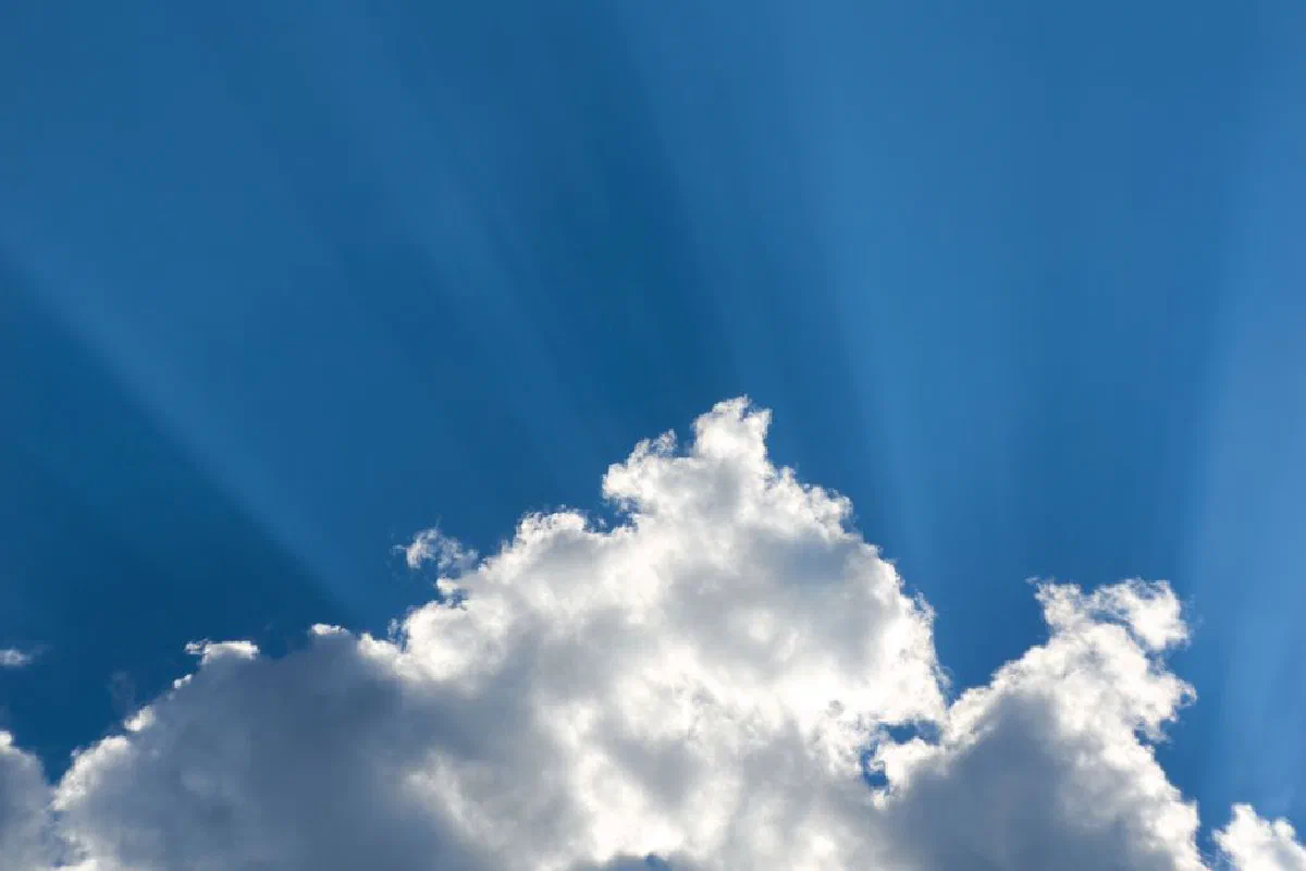 Cumulus clouds illuminated by sunbeams against a vibrant blue sky, creating a dramatic and serene atmosphere.