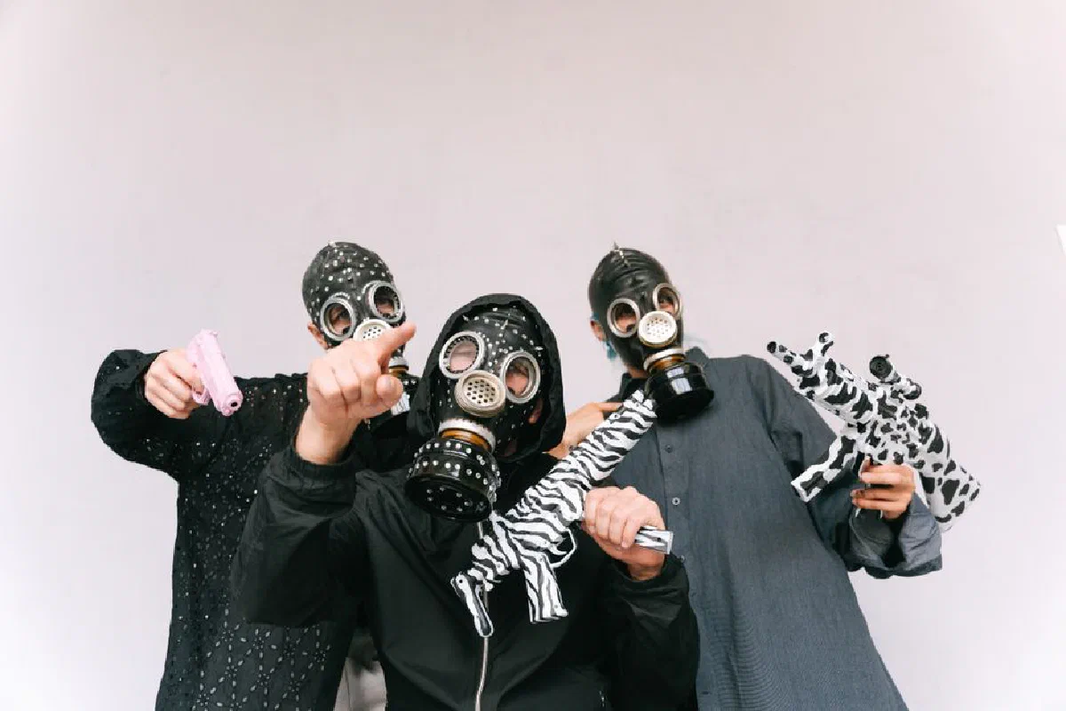 Three masked individuals pose with toy weapons, showcasing artistic costumes.