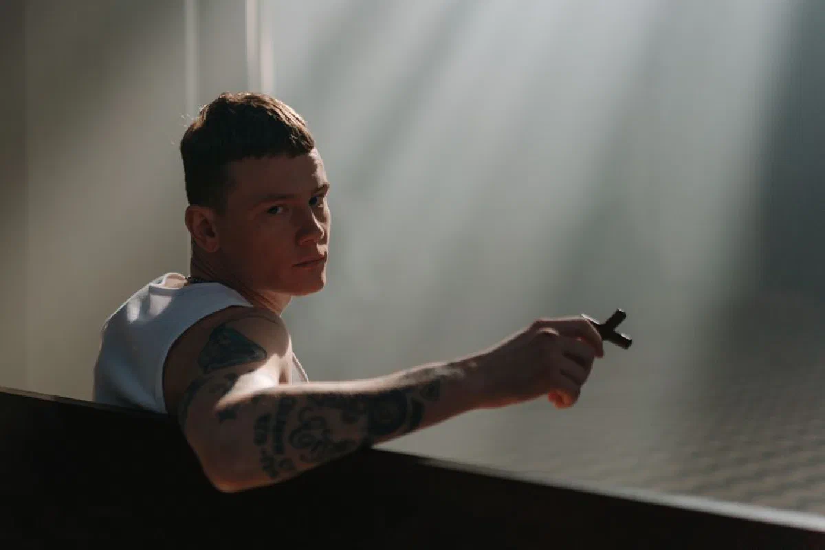 A tattooed man holding a cross in a sunlit church, conveying spirituality.