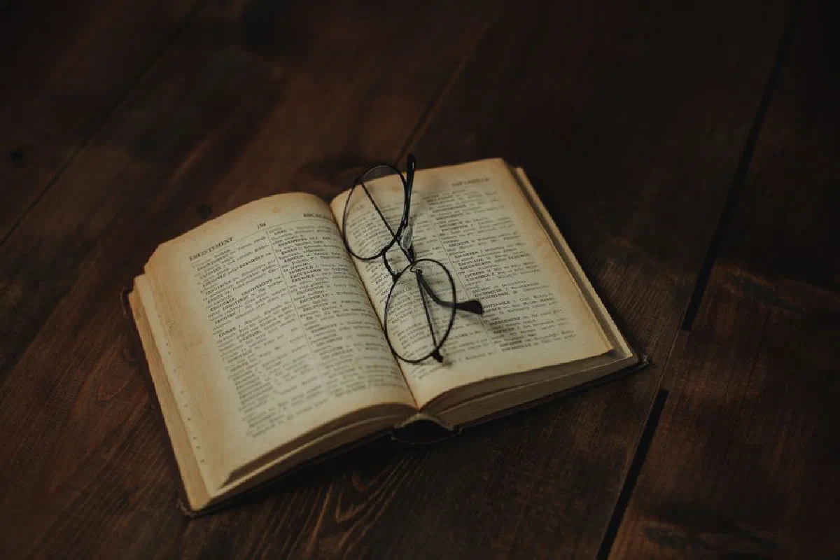 Open vintage book with eyeglasses resting on a wooden surface, evoking a sense of nostalgia.
