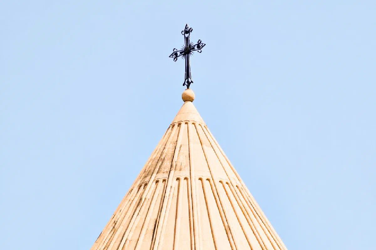 Close-up of a church steeple with a cross against a clear blue sky, showcasing architectural details.