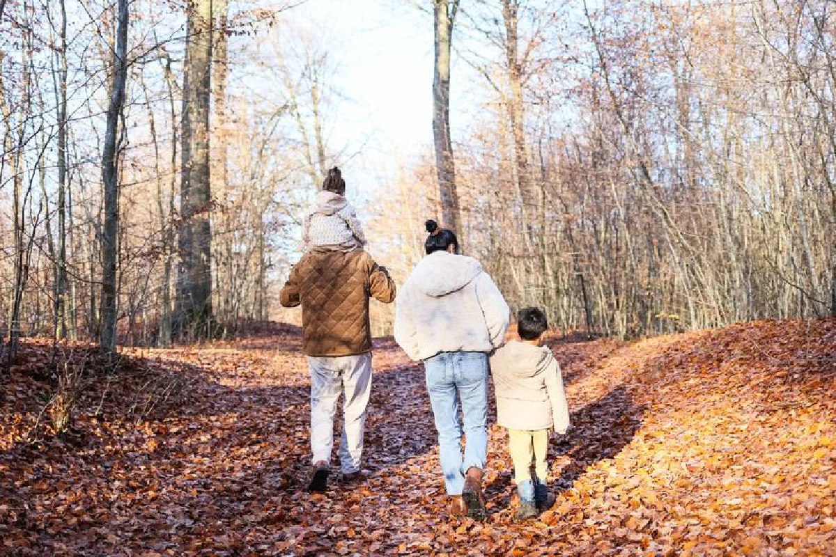 A family of four strolling on a leaf-covered path in a fall forest.