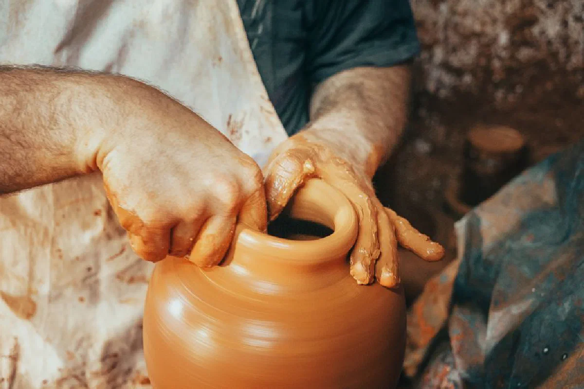 Artisan craft person shaping a clay pot on a spinning pottery wheel with expertise.