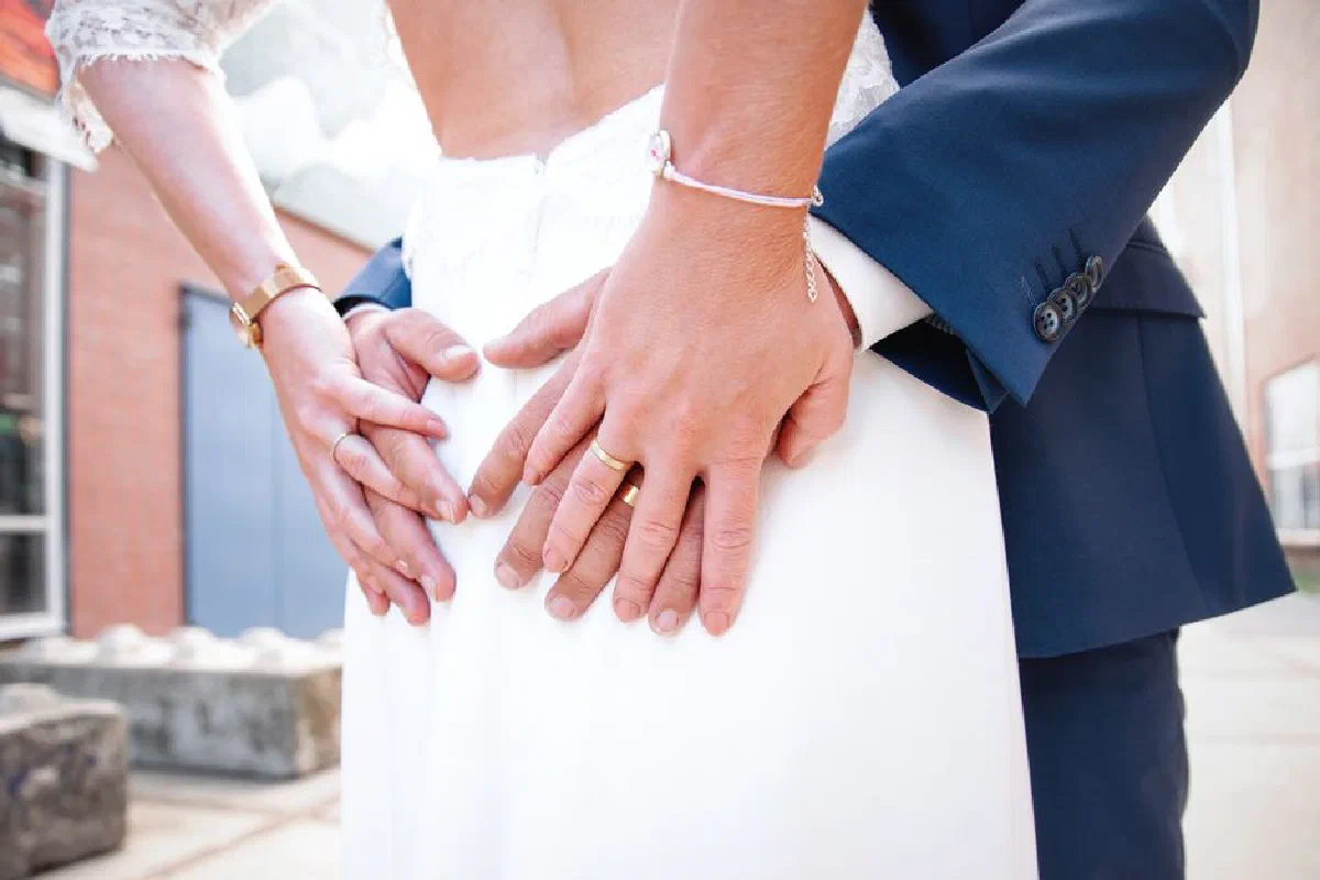 Tender moment between bride and groom, focusing on hands and wedding rings, showcasing love and commitment.