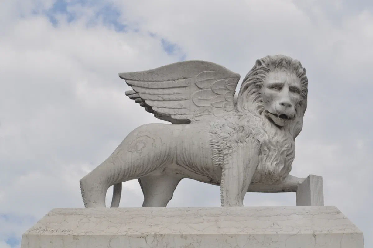 A stunning marble statue of a winged lion set against a cloudy sky.