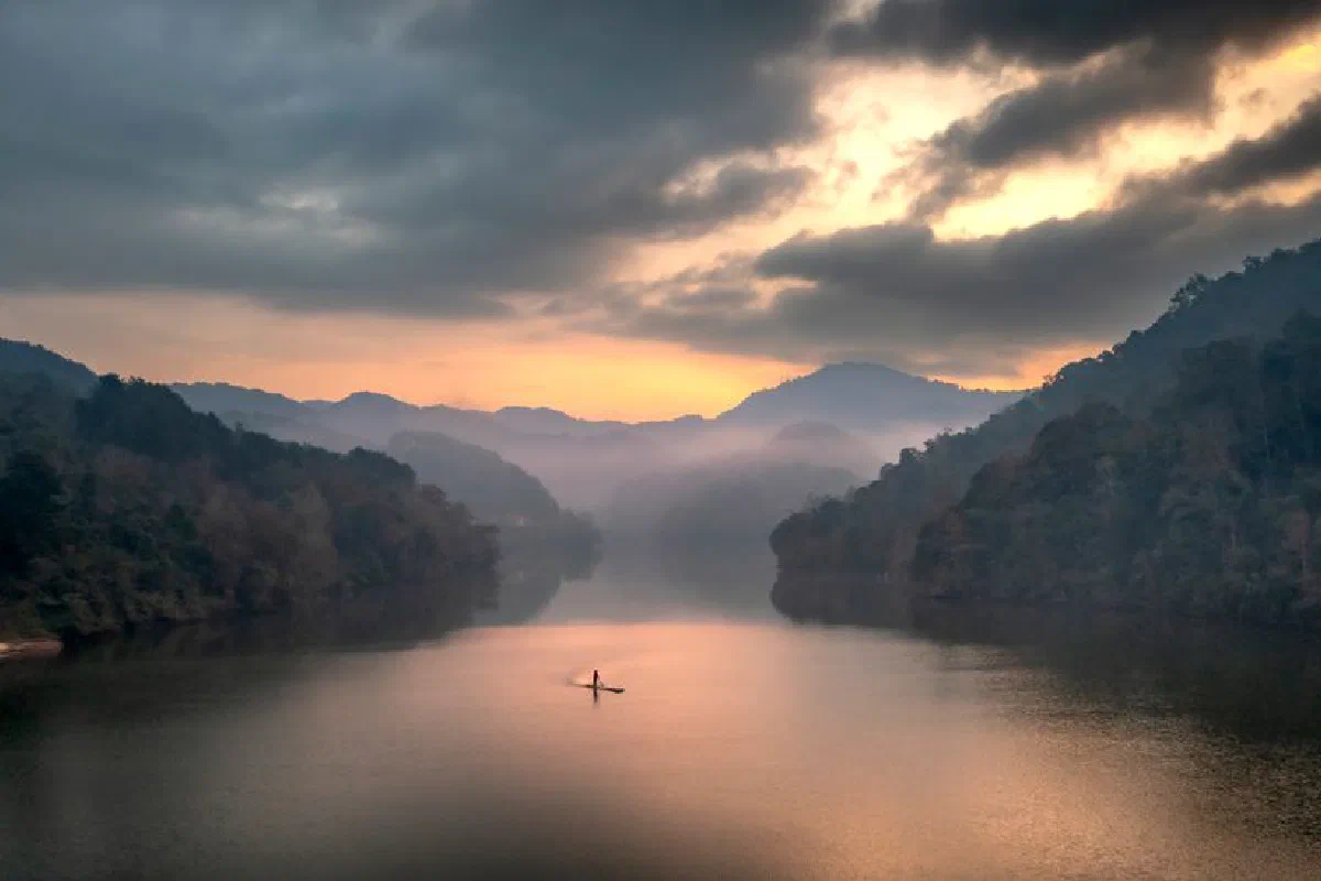 A tranquil scene of a lone boat on a lake surrounded by mountains at sunset.