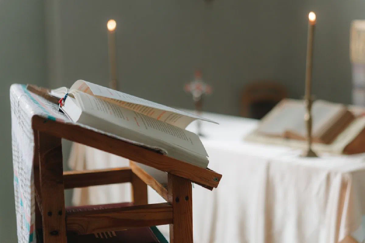 Open Bible placed on a wooden podium in a tranquil church setting with lit candles.