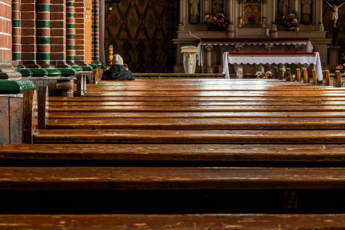 Empty church interior with wooden pews leading to richly decorated altar, warm atmosphere.