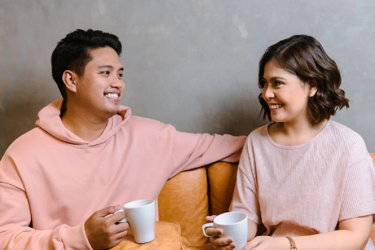 A happy couple sharing a moment with coffee cups, indoors in a cozy setting.