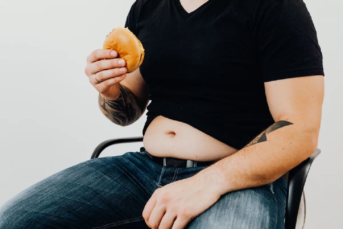 Adult man sitting with a burger. Casual style with tattoos and denim jeans.