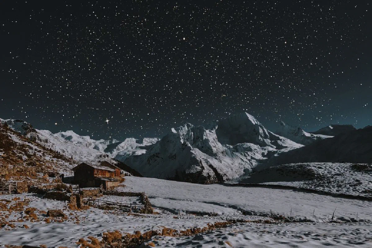 A breathtaking starry night over a snow-capped mountain landscape with a rustic cabin.