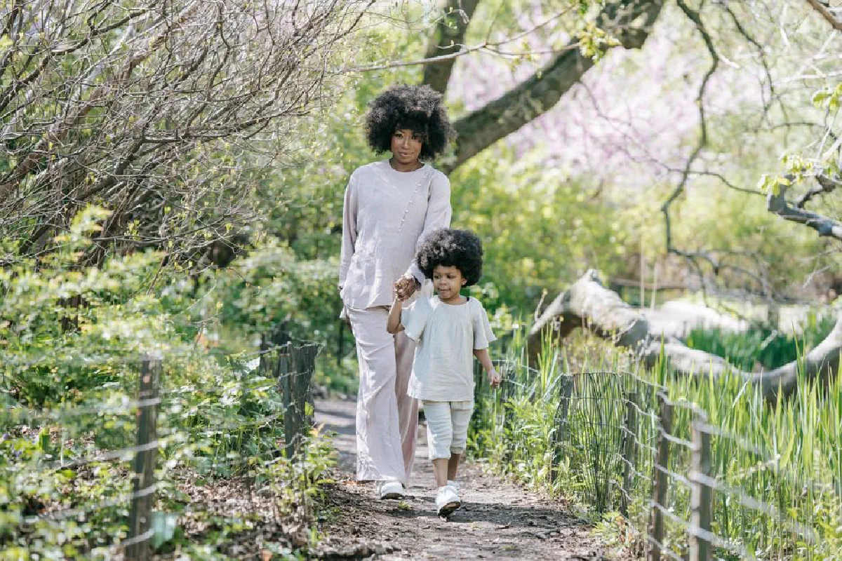 A mother and daughter walk hand in hand along a lush, sunlit path in spring.