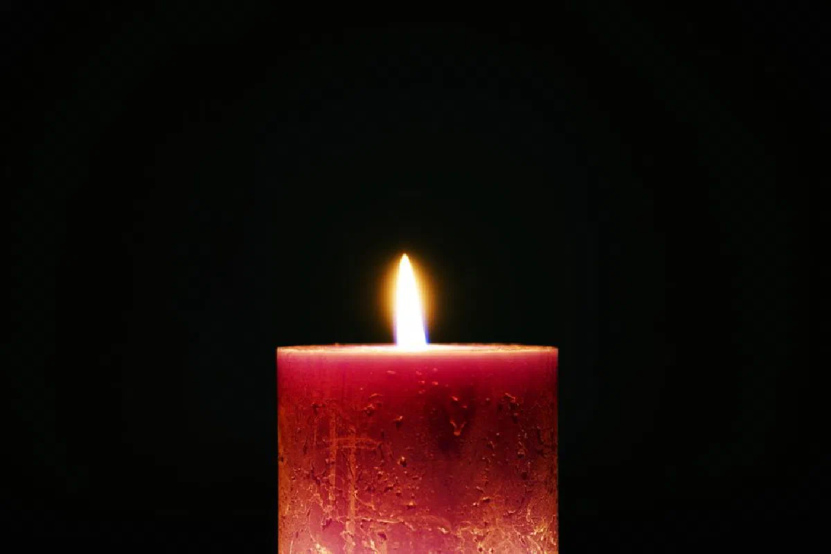 A solitary red candle with a bright flame against a dark background, creating a serene atmosphere.