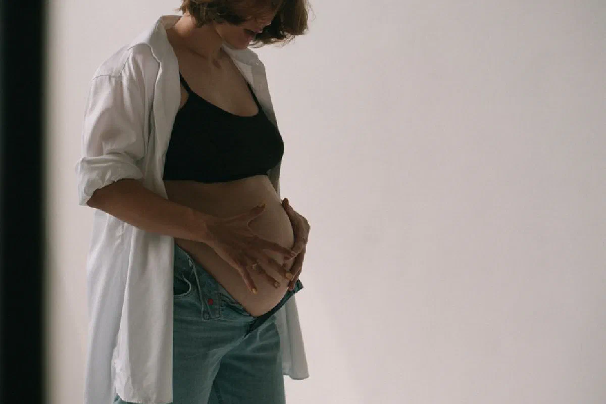 A pregnant woman in casual attire gently embraces her belly, highlighting the beauty of maternity.