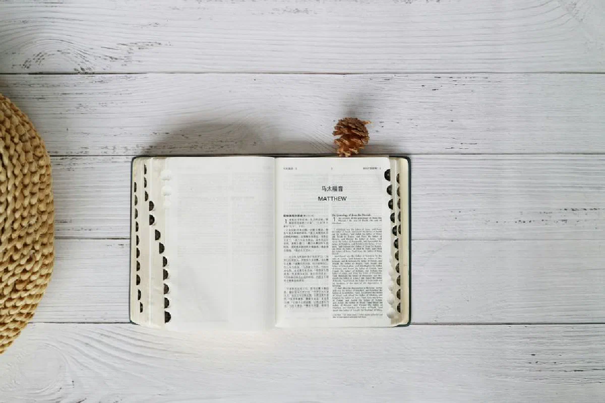 An open Bible on a white wooden table, top view, with ample copyspace.