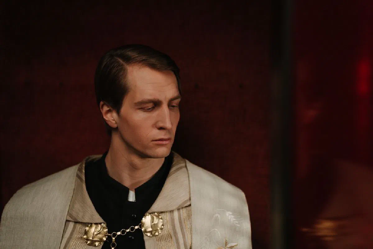 A priest in traditional vestments within a dimly lit confessional booth, showing serenity.