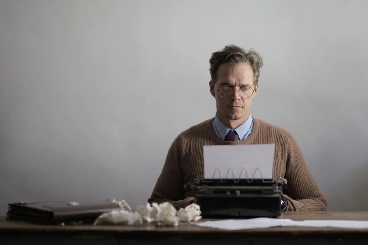 A thoughtful male writer typing on a vintage typewriter, surrounded by crumpled papers.