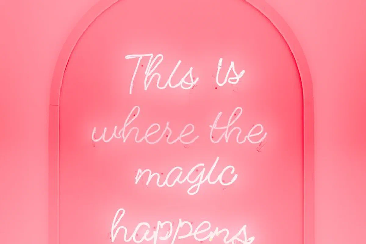 Bright pink neon sign saying 'This is where the magic happens'.