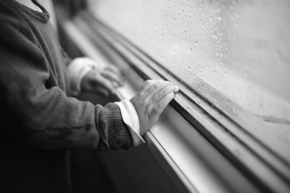 A child's hand touching a rainy window, expressing curiosity and solitude.