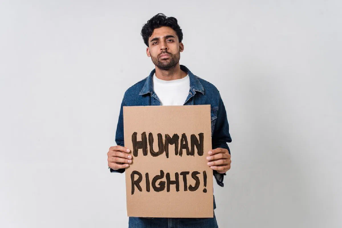 A man in a denim jacket holding a cardboard sign promoting human rights.