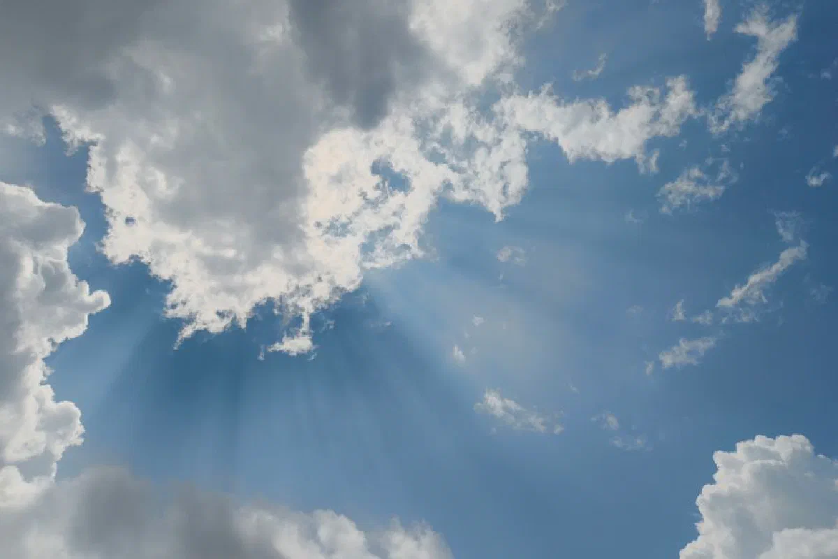 Dramatic sunrays pierce through scattered clouds on a clear day, creating a heavenly scene.