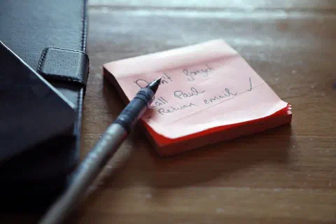 A close-up of sticky notes with a to-do list, a pen, and a wallet on a wooden desk.