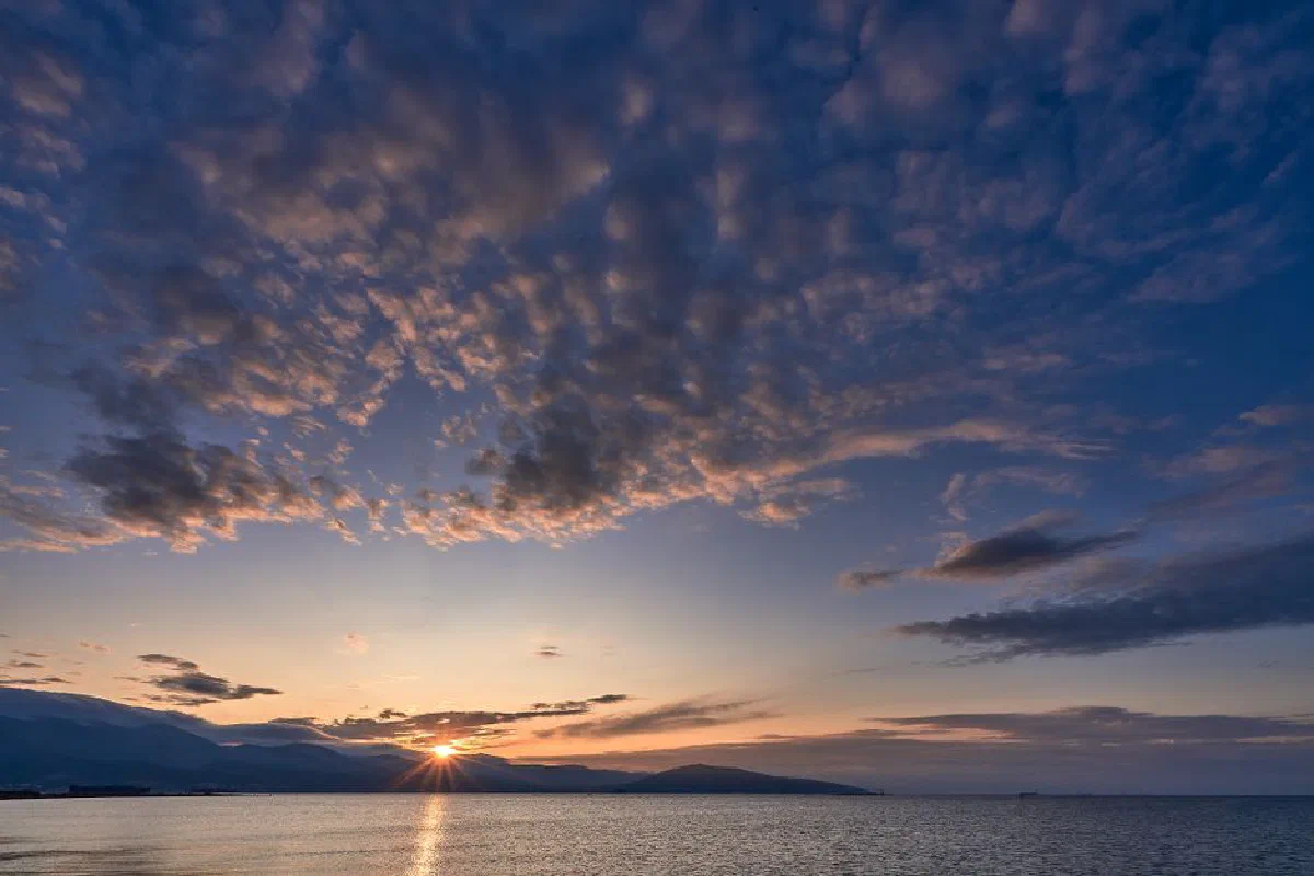 Breathtaking sunrise over the calm waters of Novorossiysk, Russia, with vibrant sky and mountains.