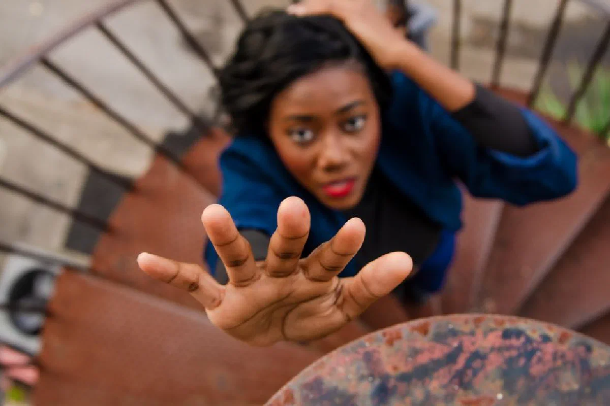 Woman extending hand while climbing spiral staircase, symbolizing struggle or help-seeking.