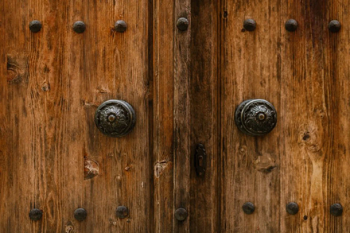 Close-up of a rustic wooden door with ornate knobs and a weathered texture.