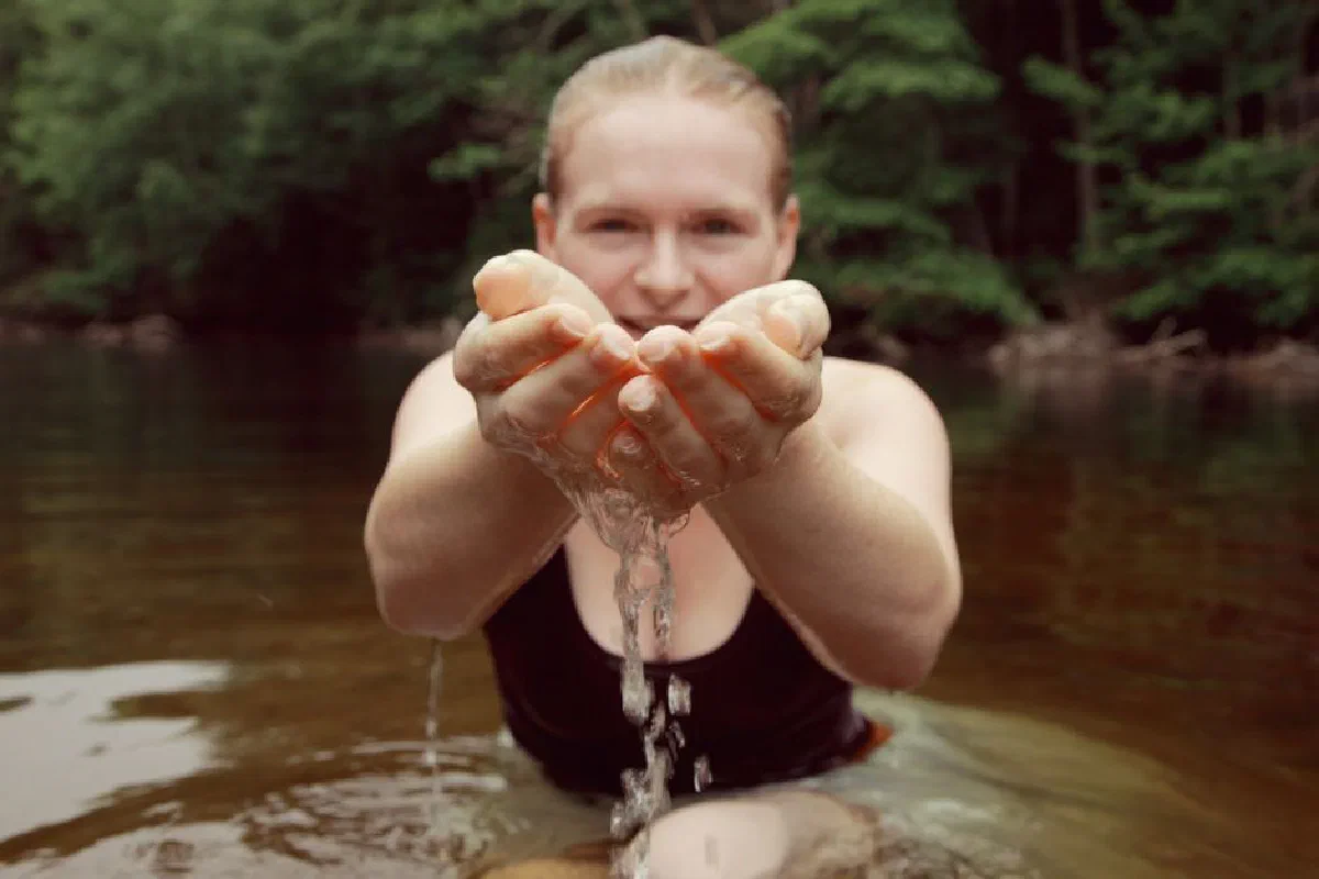 A woman in a black tank top enjoying natural water in a serene river setting.