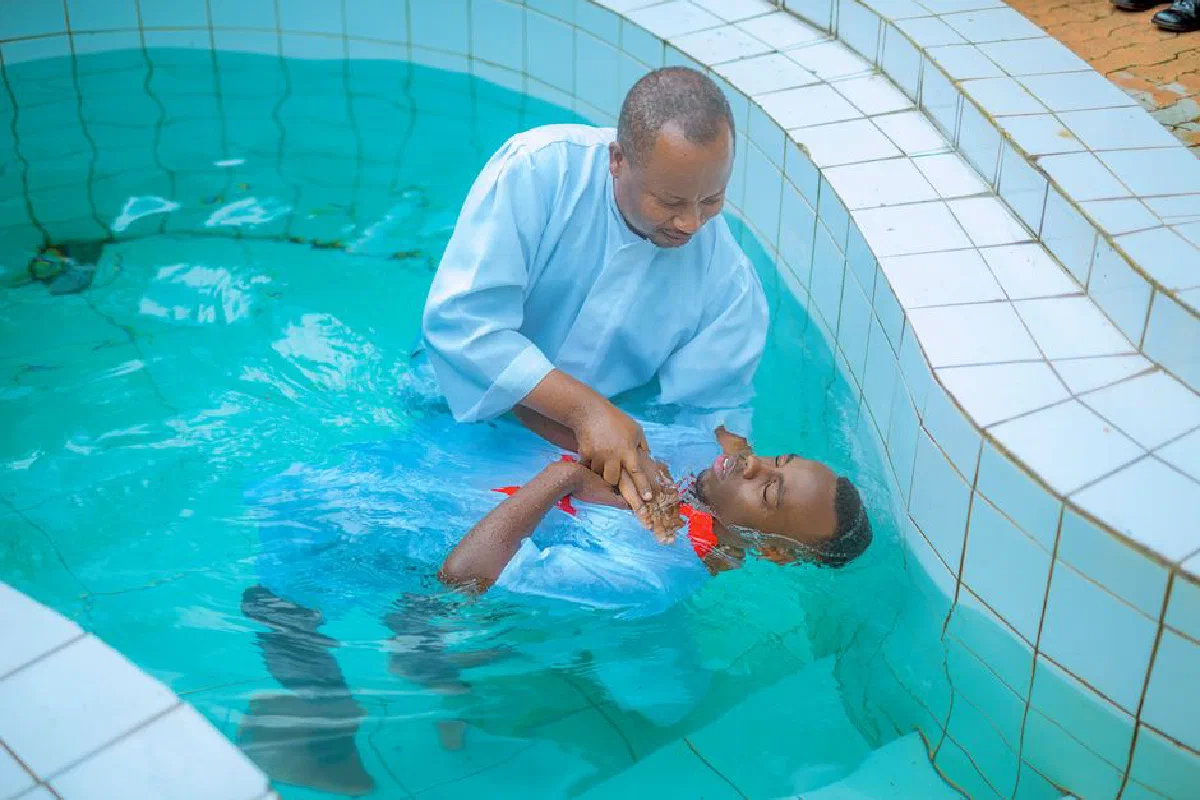 Man and child participating in a baptism ceremony in a pool setting, captured outdoors.