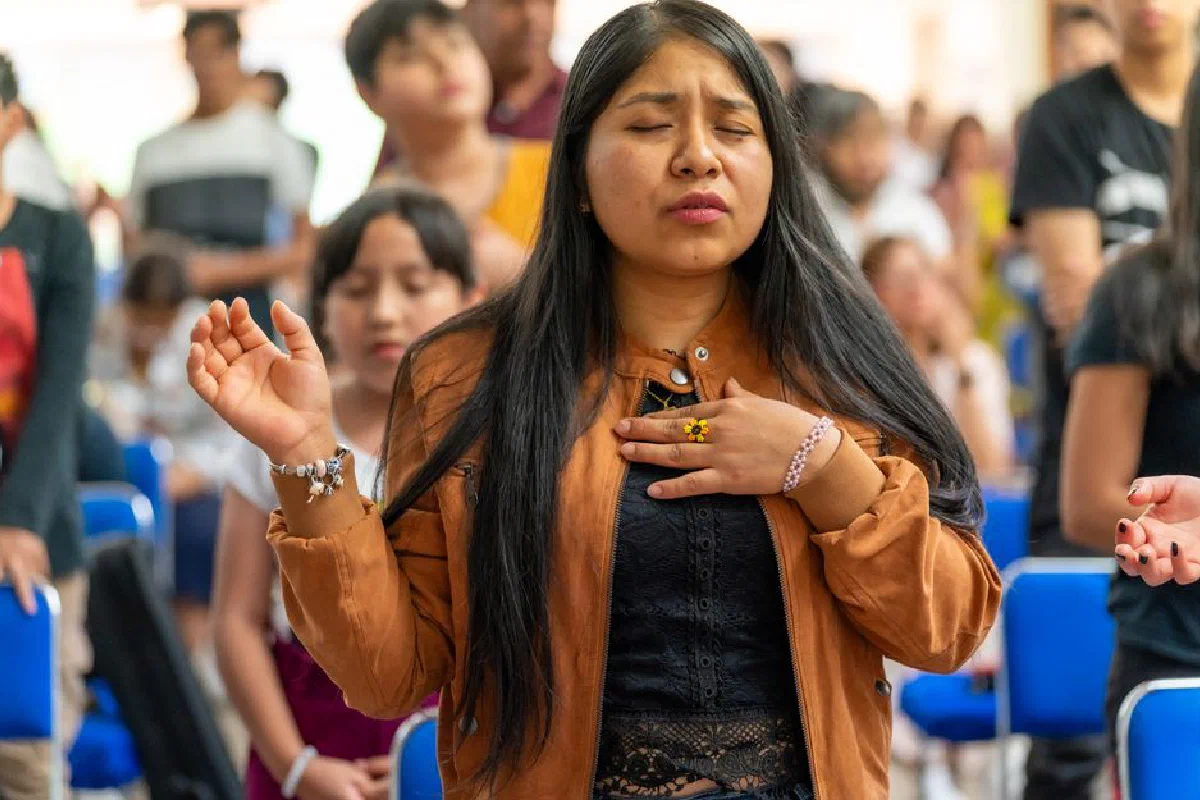 A woman with eyes closed, deeply engaged in prayer during a church service in Mexico City, filled with spirituality.