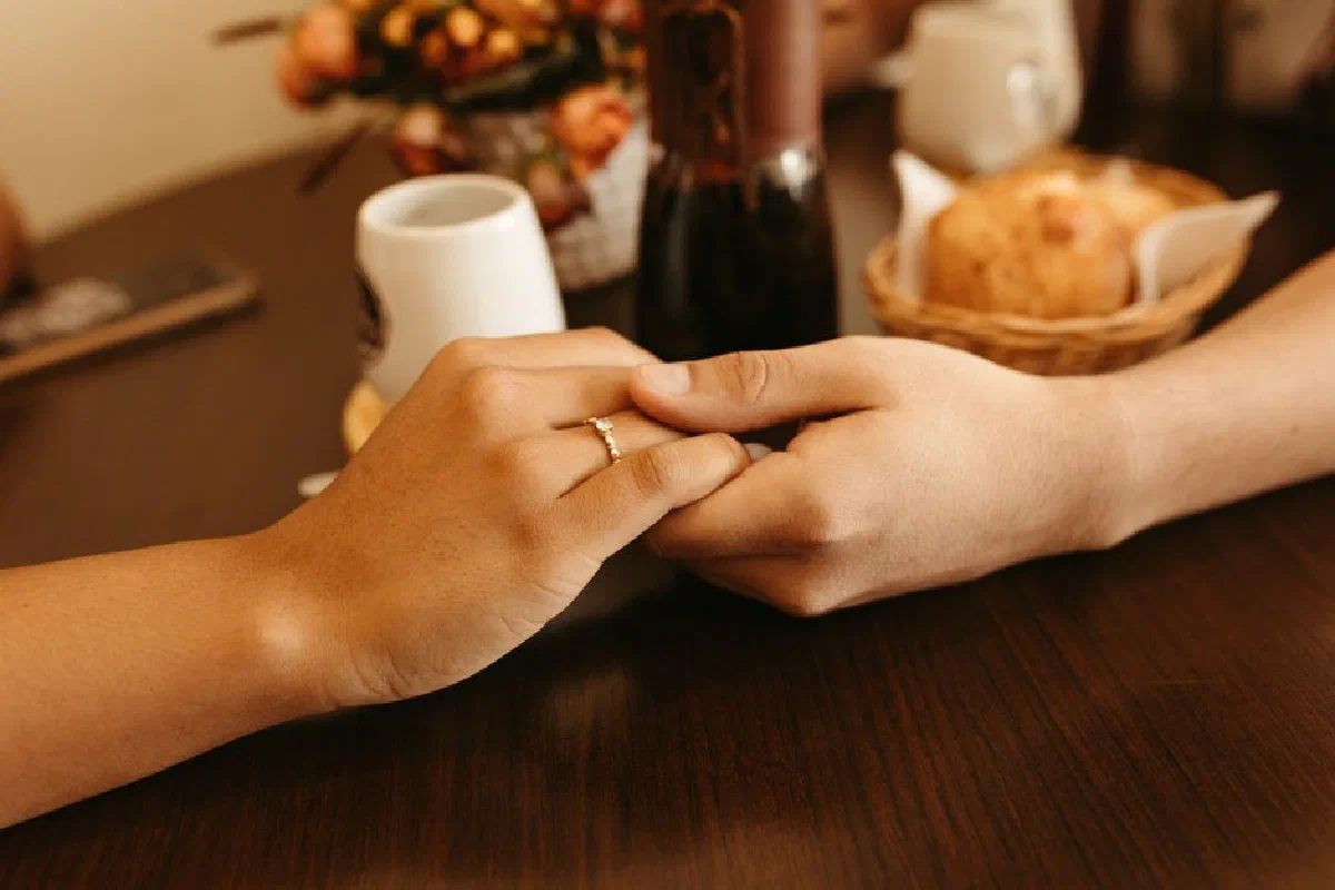 Close-up of a romantic couple holding hands at a café table, highlighting an engagement ring.