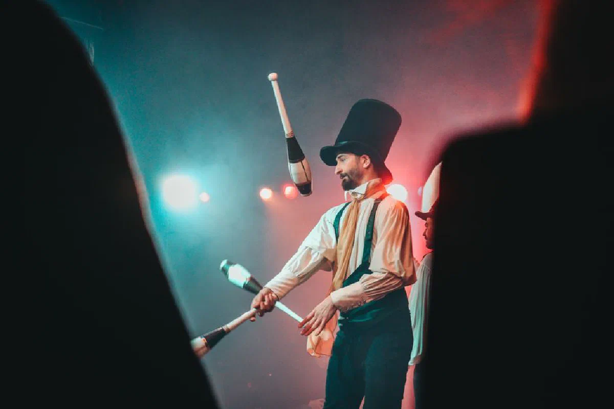 Juggler in top hat skillfully performing under colorful stage lights.