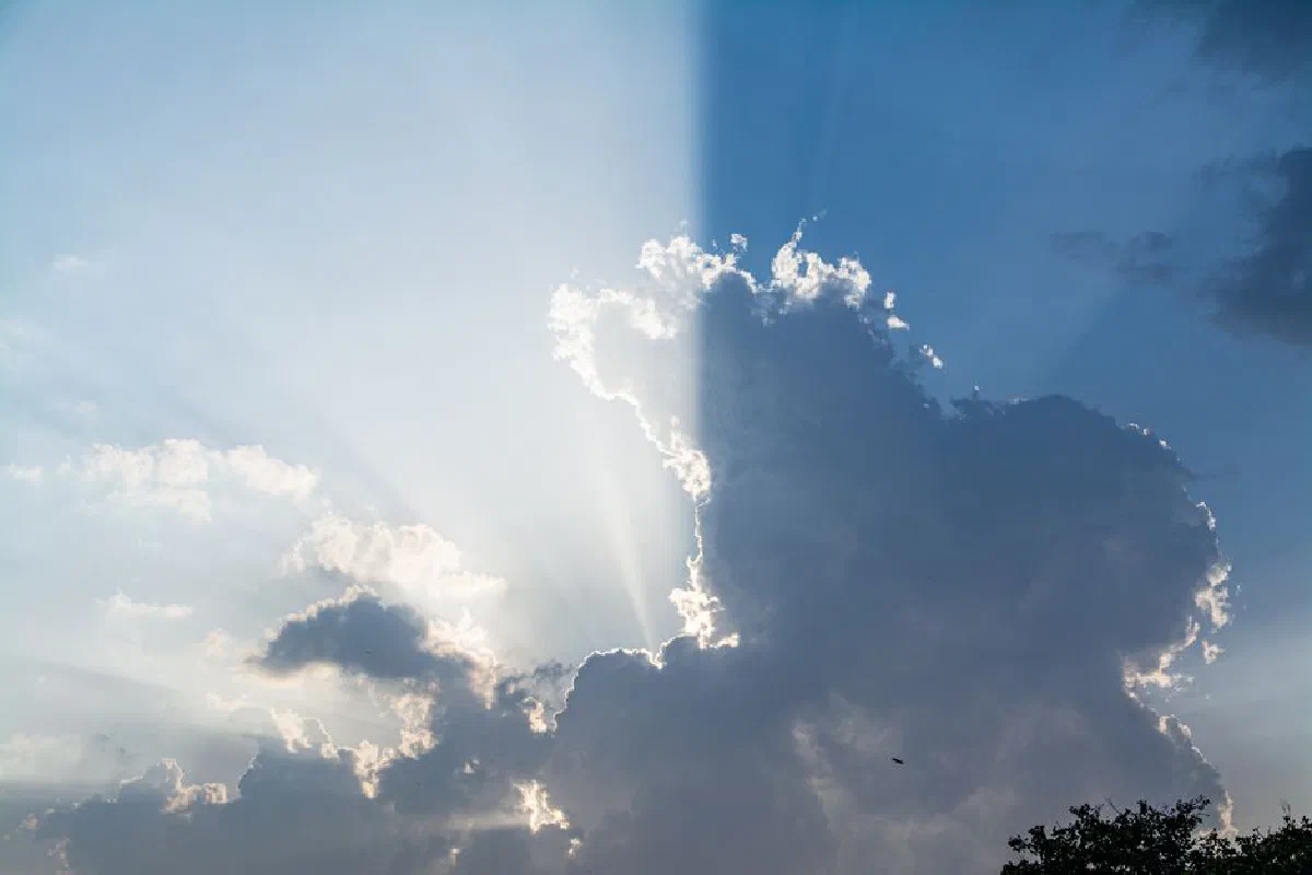 A stunning view of sun rays breaking through dramatic clouds in a clear blue sky.