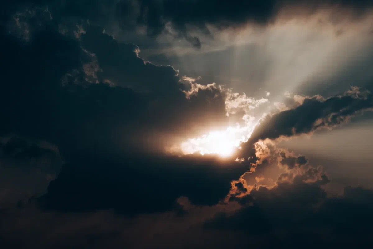 Sunlight beams piercing through dark clouds, creating a dramatic sky scene.