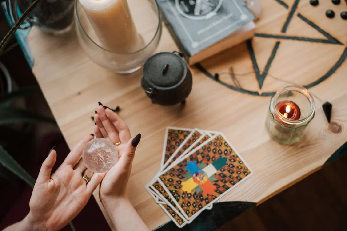 From above of crop unrecognizable fortune teller with crystal ball at table with tarot cards during divination process