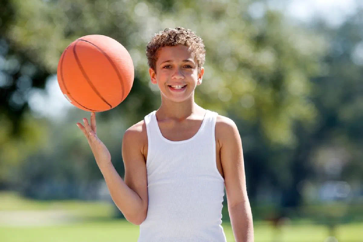Smiling boy spinning basketball on finger in a sunny outdoor park.