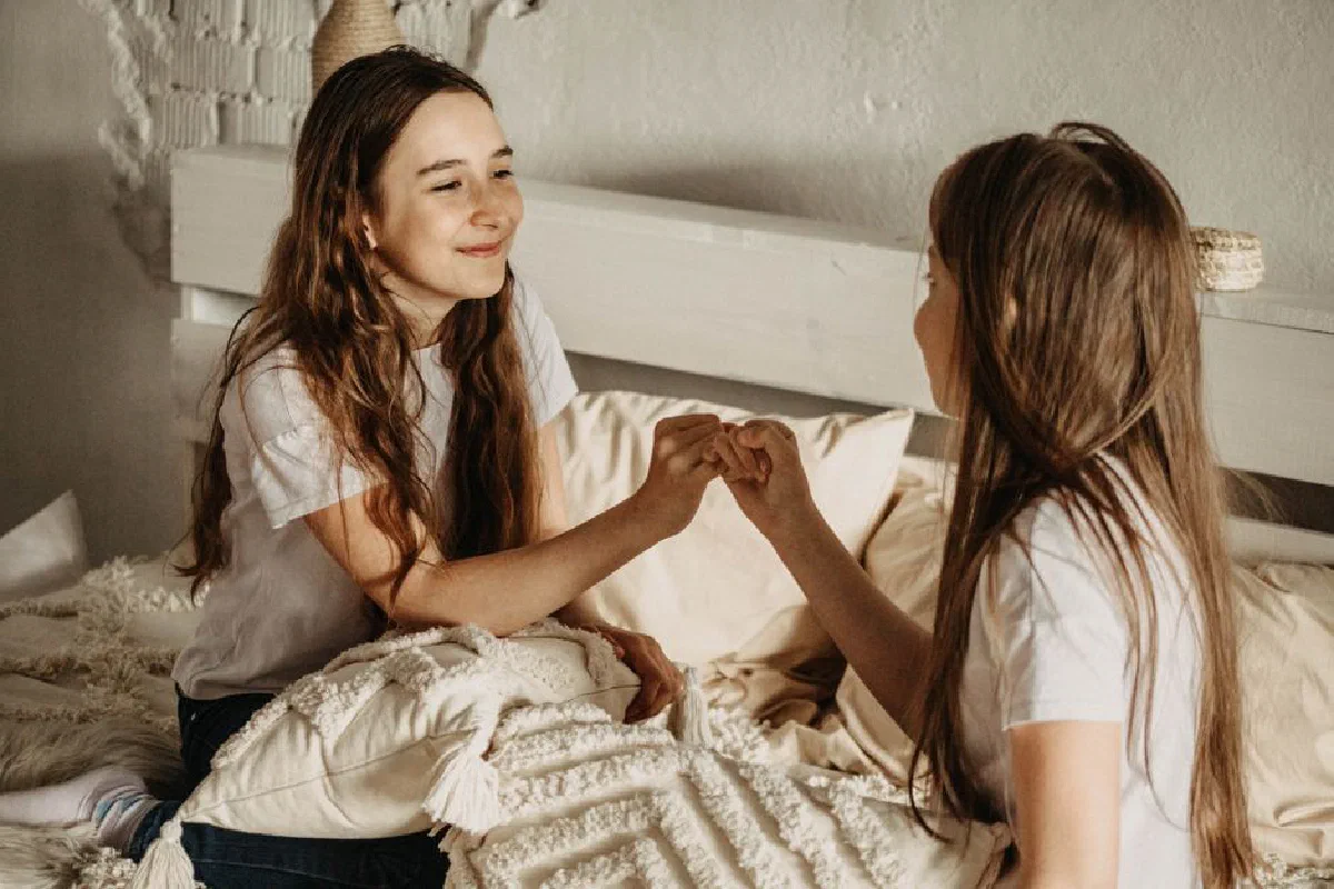 Teenage girls sitting on bed, engaged in a happy and serene moment of friendship.