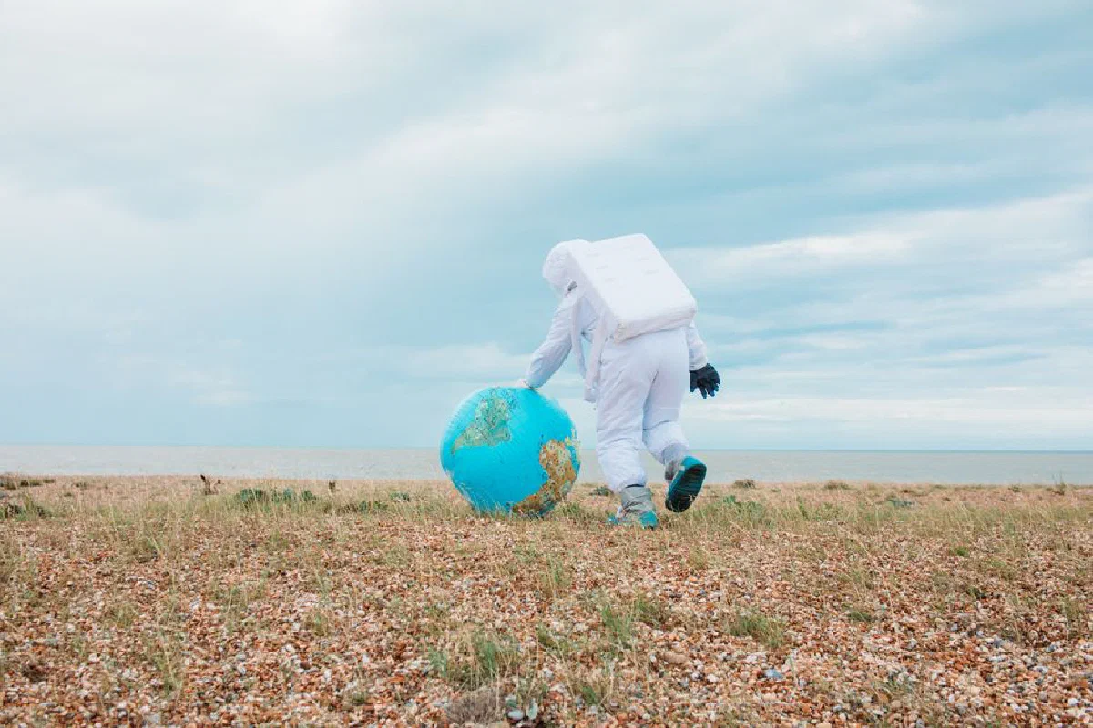 Astronaut in space suit walking on a pebbled beach with an inflatable Earth globe.