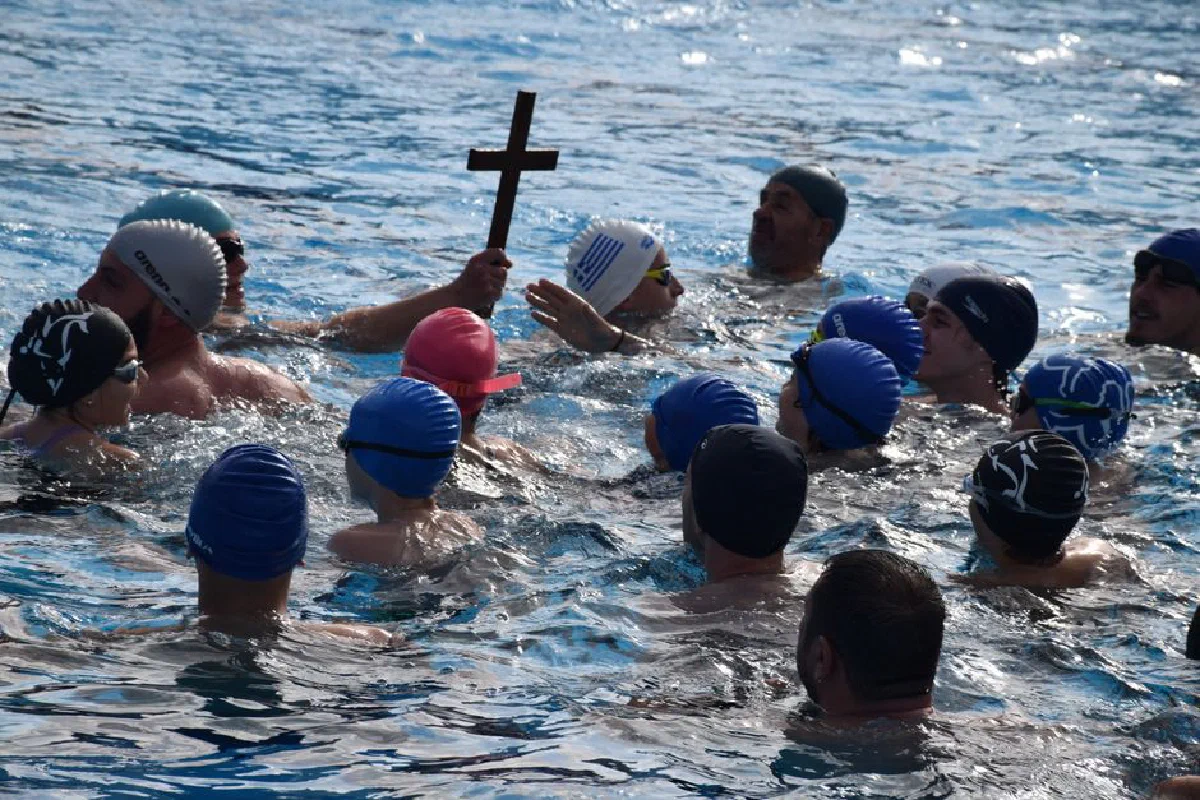 Swimmers gather in a pool with one holding a cross, symbolizing a religious ceremony.