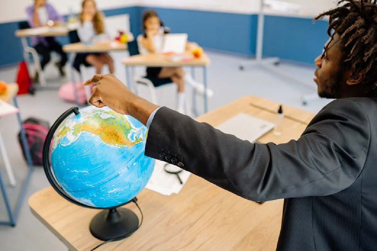 A teacher points to a globe in a classroom, engaging students in a geography lesson.