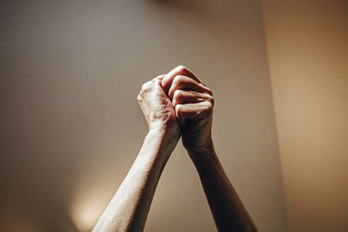 Crop anonymous middle aged man and woman with clasped hands and shiny skin on arms near smooth wall at home in daylight